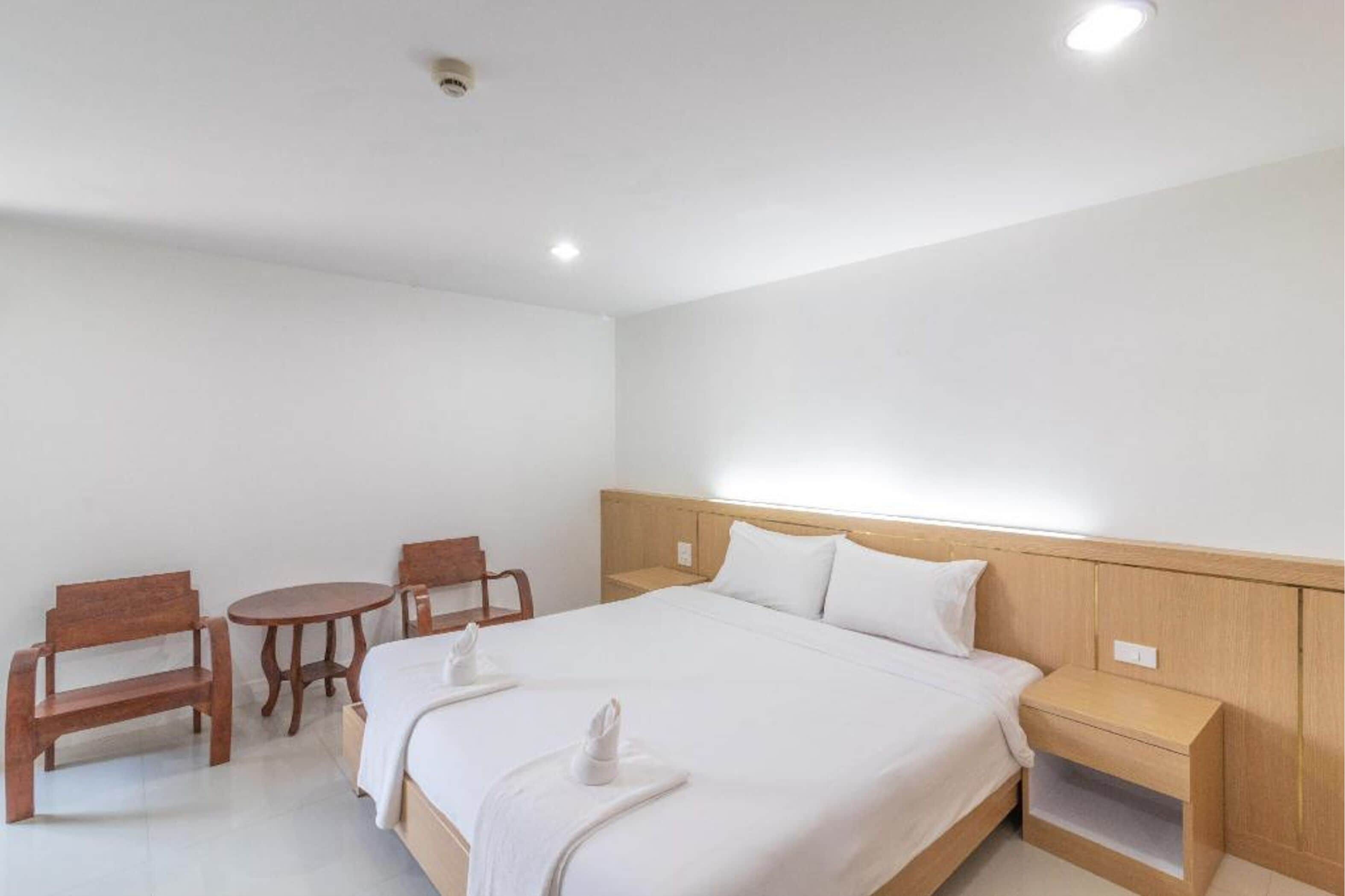 A hotel room with a large bed, wooden nightstands, a small round table, and two wooden chairs.