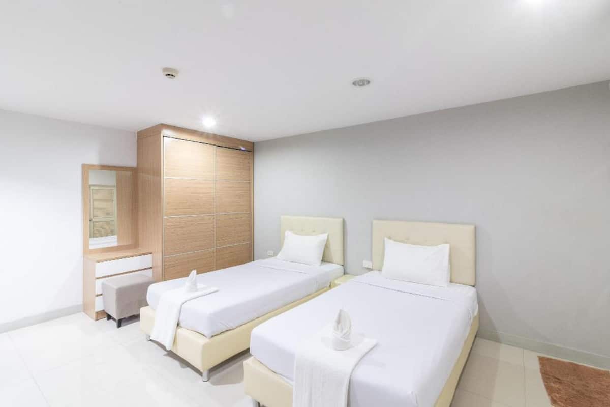 A hotel room with two beds, a wooden wardrobe, a small seating area, and a mirror.