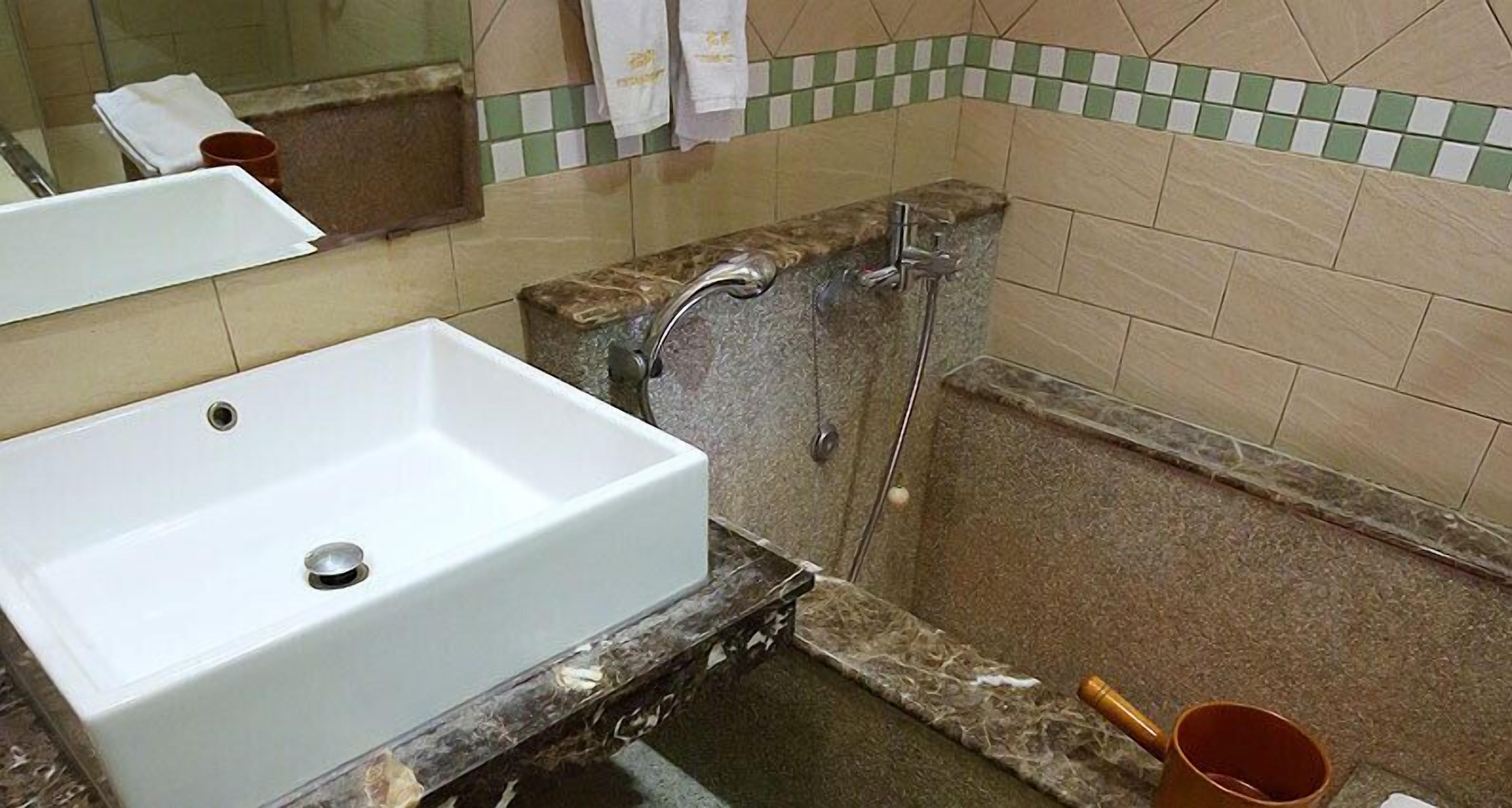 Une salle de bain avec un lavabo blanc, un espace douche et un mur carrelé.