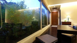 A hotel room with a large glass window, a wooden desk, a small rug, and a door leading to another room. - Yi Yuan Resort (Shoufeng)