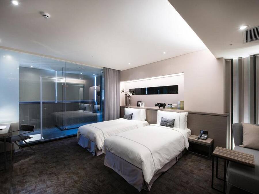 Une chambre d’hôtel moderne équipée de deux lits, d’un bureau, d’une chaise, d’une petite table, d’une table de chevet et d’une cabine de douche en verre.