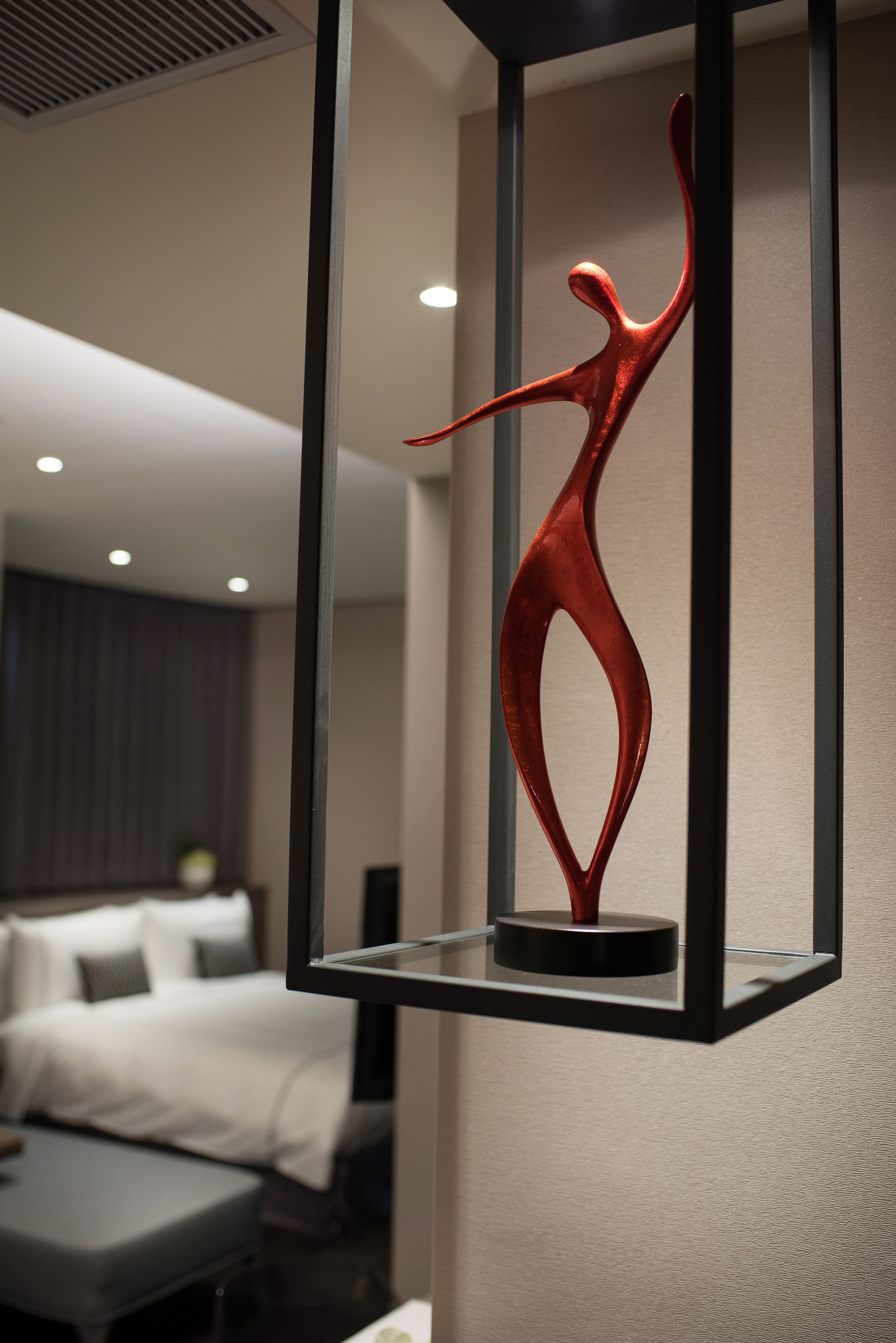 Quarto de hotel moderno com cama, mesa de cabeceira e uma escultura decorativa vermelha numa moldura preta.
