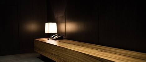 Un banco de madera con un teléfono y una lámpara en una habitación con poca luz.