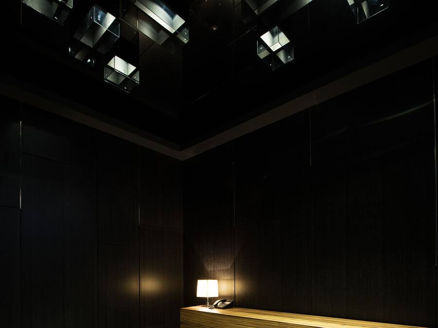 Una habitación con poca luz, un banco de madera y una lámpara de mesa.