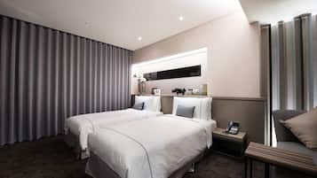 A hotel room with two beds, a bedside table with a phone, a small table with a vase, and a large window with curtains.