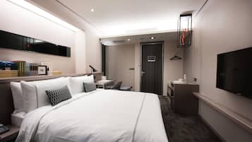 A hotel room with a large bed, a desk, a chair, a TV, and a wardrobe.