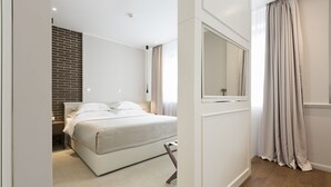 A modern bedroom with a bed, a large mirror, and a view of a brick wall. - Envoy Hotel Belgrade (Belgrade)