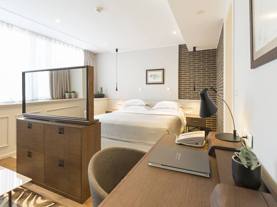 A modern hotel room with a bed, desk, chair, and a large mirror.