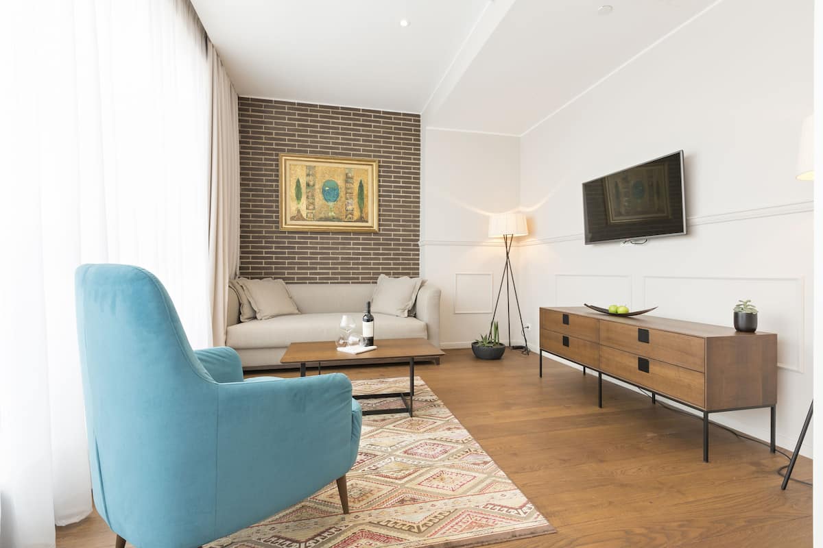 A modern living room with a blue armchair, a sofa, a coffee table, a wooden cabinet, and a flat-screen TV mounted on the wall.