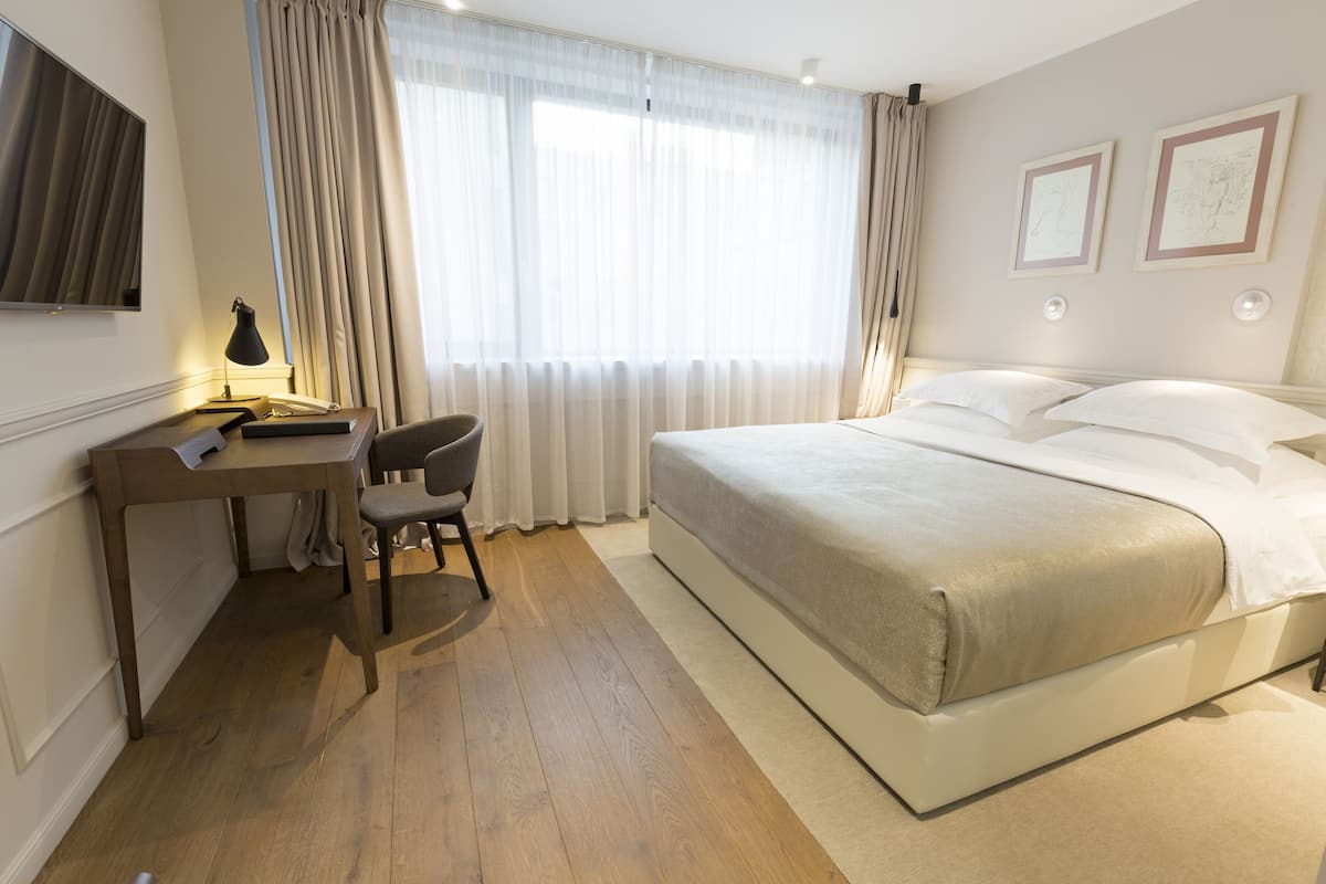 A hotel room with a bed, a desk with a chair, a TV, and curtains.