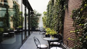 An outdoor patio with tables and chairs, surrounded by a brick wall covered in ivy. - Envoy Hotel Belgrade (Belgrade)