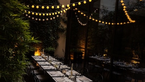 A long dining table set for multiple guests, surrounded by chairs, with string lights overhead. - Envoy Hotel Belgrade (Belgrade)
