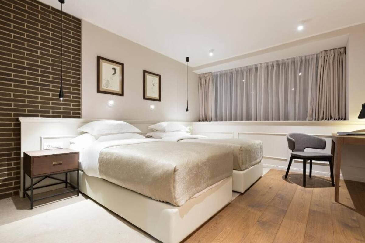 A modern bedroom with a large bed, bedside tables, a desk, and a window with curtains.
