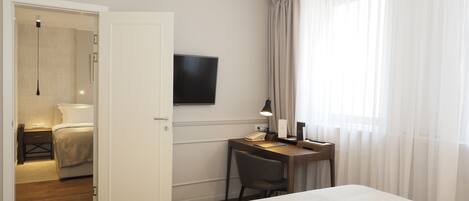 A hotel room with a bed, a desk with a chair, a TV mounted on the wall, and a window with curtains.