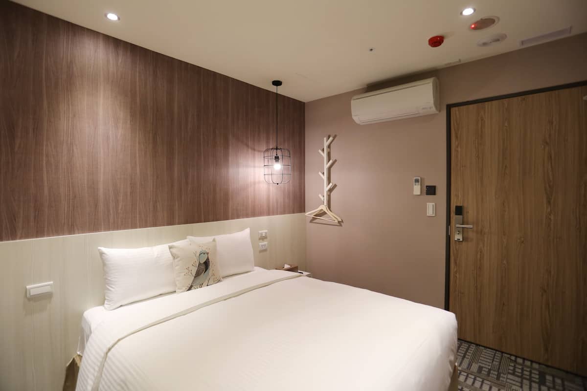 A hotel room with a large bed, wooden paneling on the walls, a wall-mounted air conditioner, and a door with a handle.