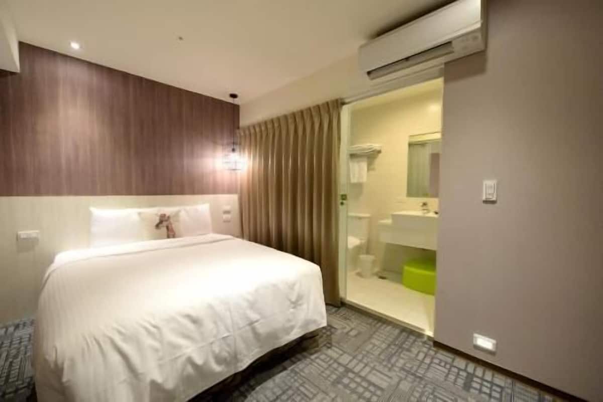 A hotel room with a bed, a bathroom with a mirror, and an air conditioning unit.
