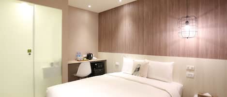 A hotel room with a bed, a desk, a chair, a nightstand, and a wall-mounted light fixture.