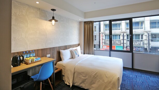 Ein Hotelzimmer mit Bett, Schreibtisch mit Stuhl, einer Kaffeemaschine und einem Fenster mit Blick auf die Stadt.