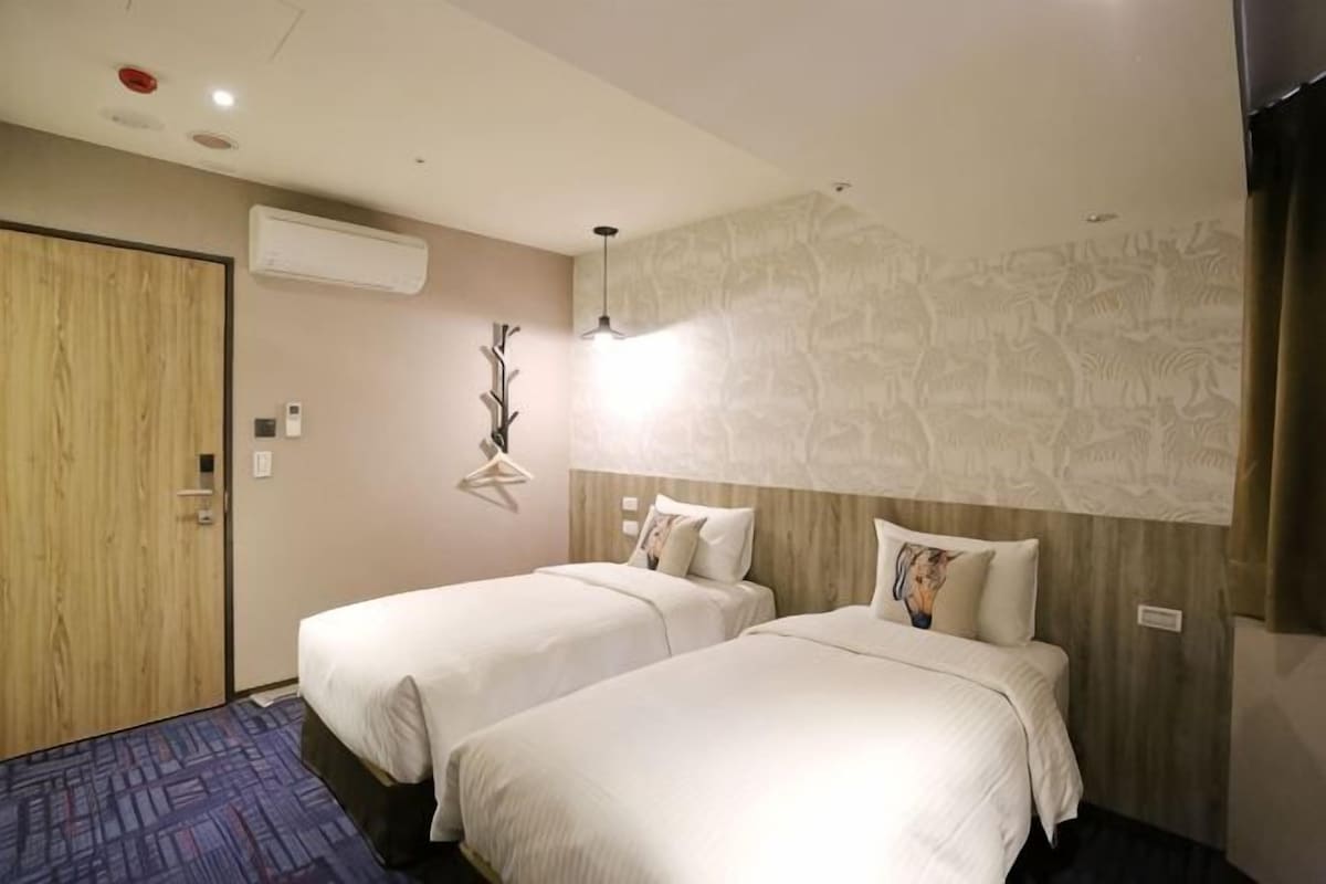 A hotel room with two beds, a wooden door, an air conditioning unit, and a wall-mounted artwork.