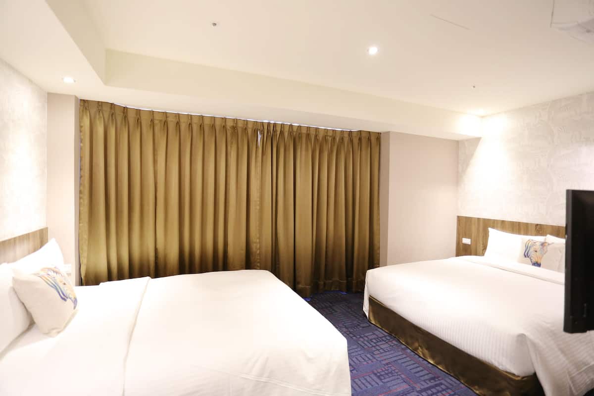 A hotel room with two beds, a large window with curtains, a flat-screen TV, and a patterned carpet.