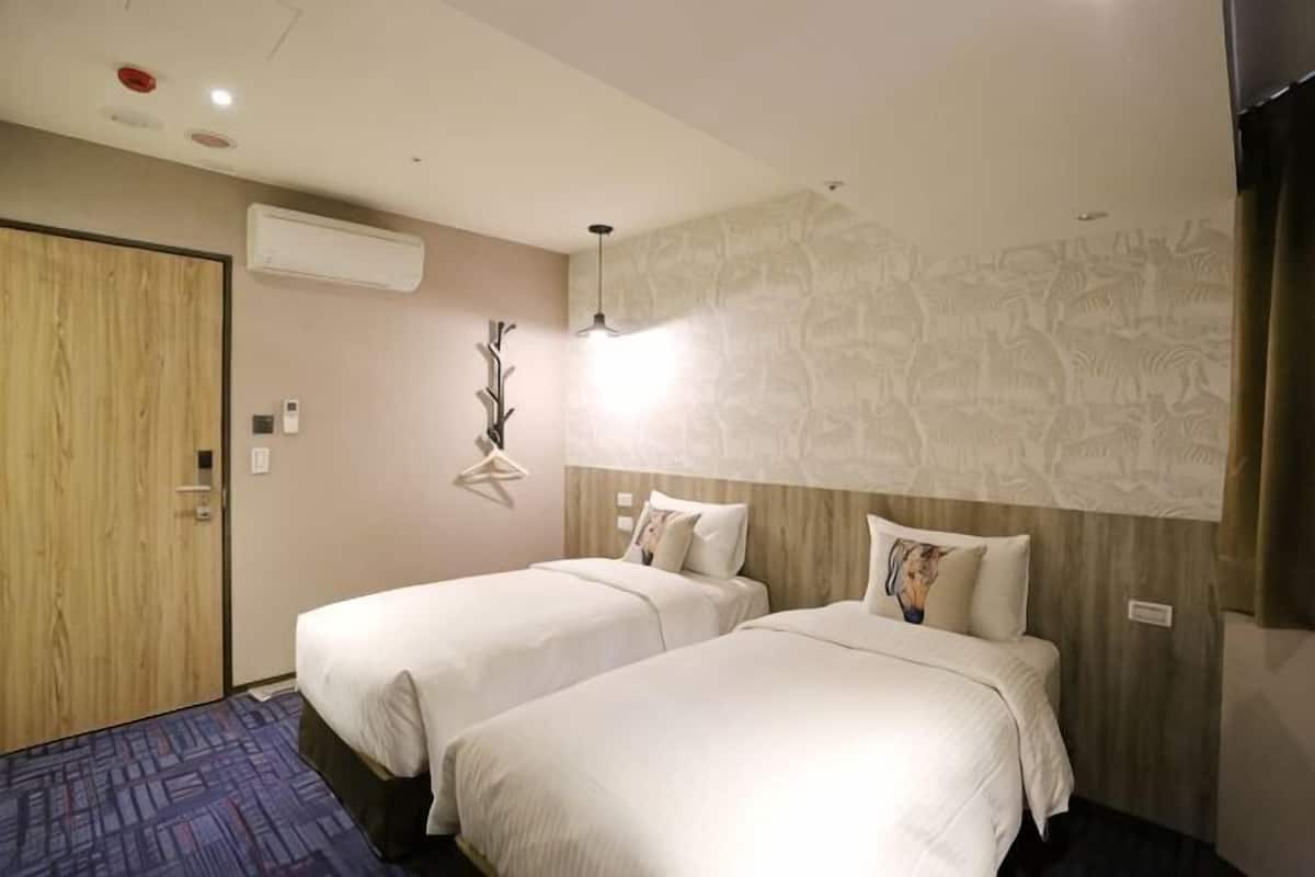 A hotel room with two beds, a wooden door, an air conditioning unit, and a wall-mounted artwork.