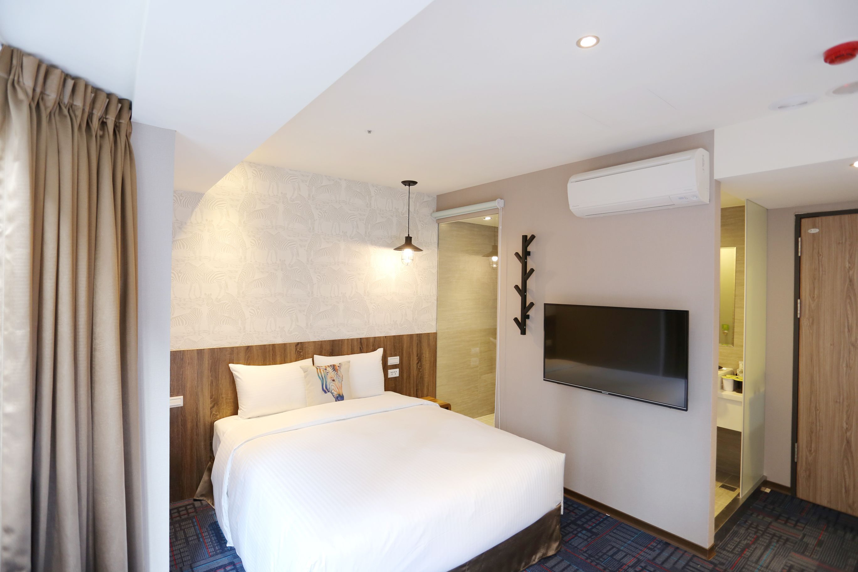 A hotel room with a large bed, a flat-screen TV mounted on the wall, an air conditioning unit, and a wooden door.