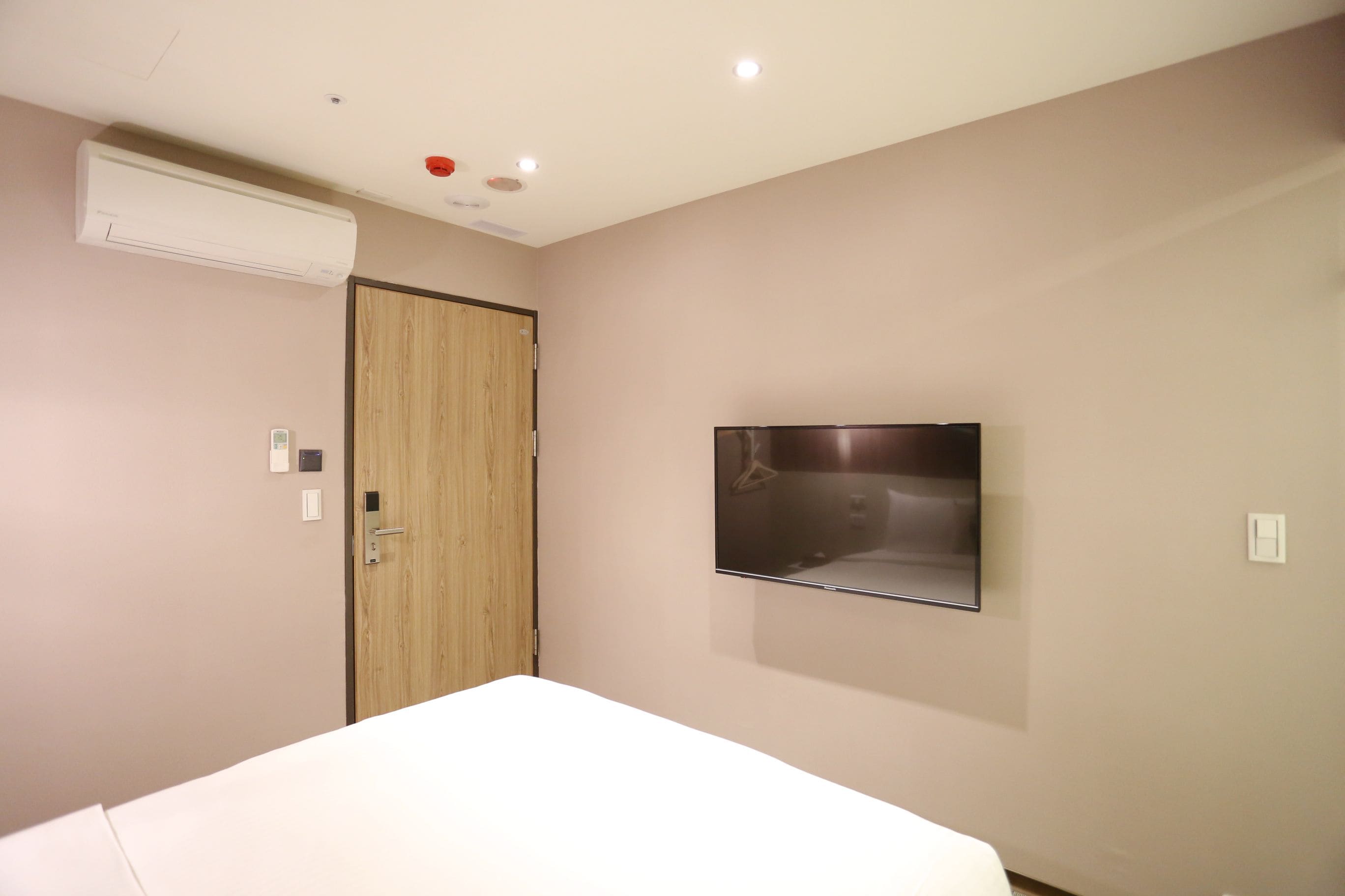 Een slaapkamer met een bed, een wandtelevisie, een airconditioning en een houten deur.