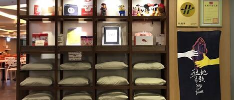 A hotel room with a large wooden shelf unit displaying various items, including pillows, a framed picture, and small figurines. There are also two framed certificates on the wall.