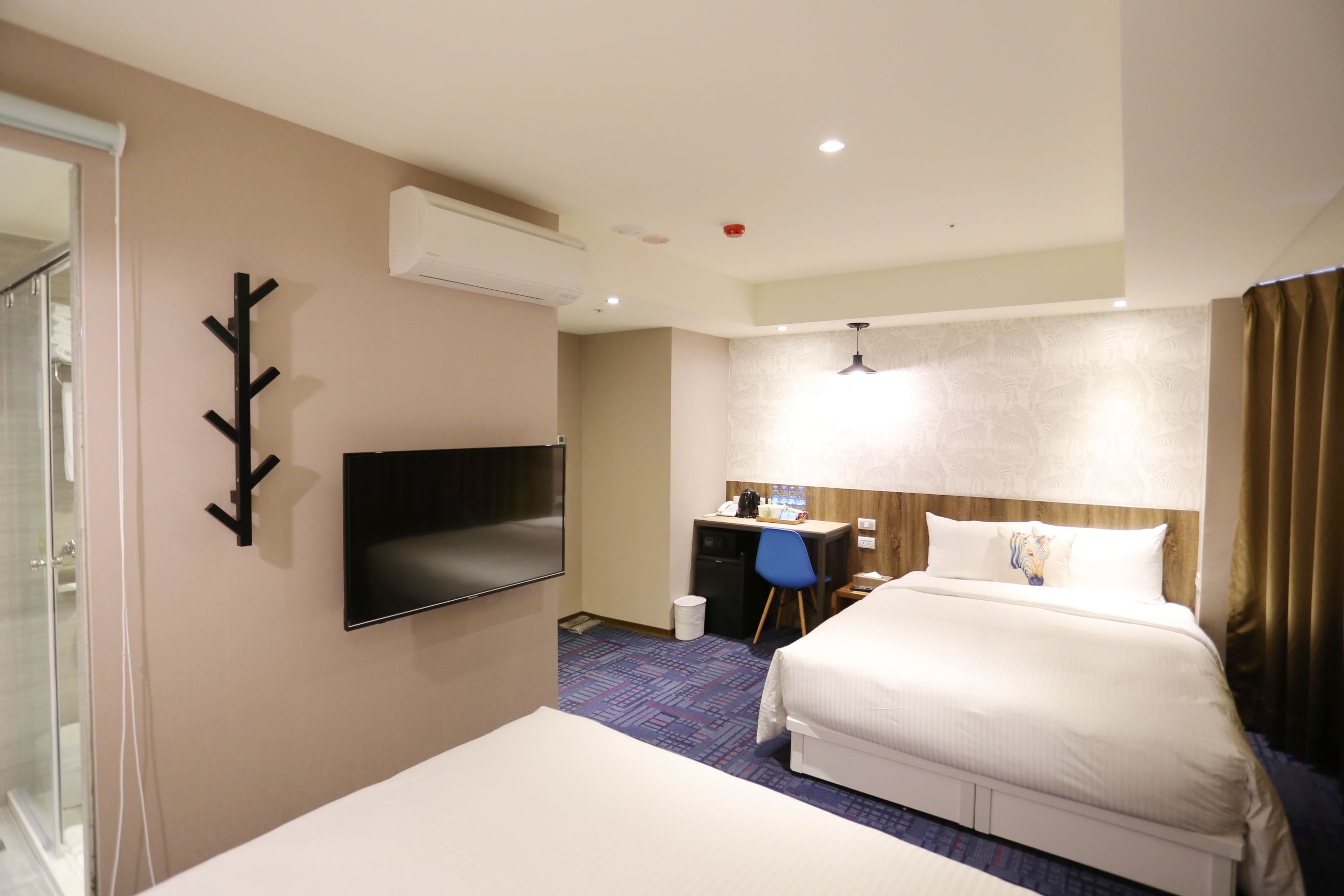 A hotel room with a bed, a desk, a chair, a TV, and a bathroom with a glass shower.