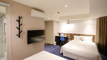A hotel room with a bed, a desk, a chair, a TV, and a bathroom with a glass shower.
