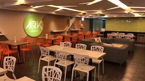 Eine moderne Hotellobby mit einer Mischung aus orangefarbenen und weißen Stühlen, einem grauen Sofa und einem großen Bildschirm, der den Namen des Hotels zeigt.