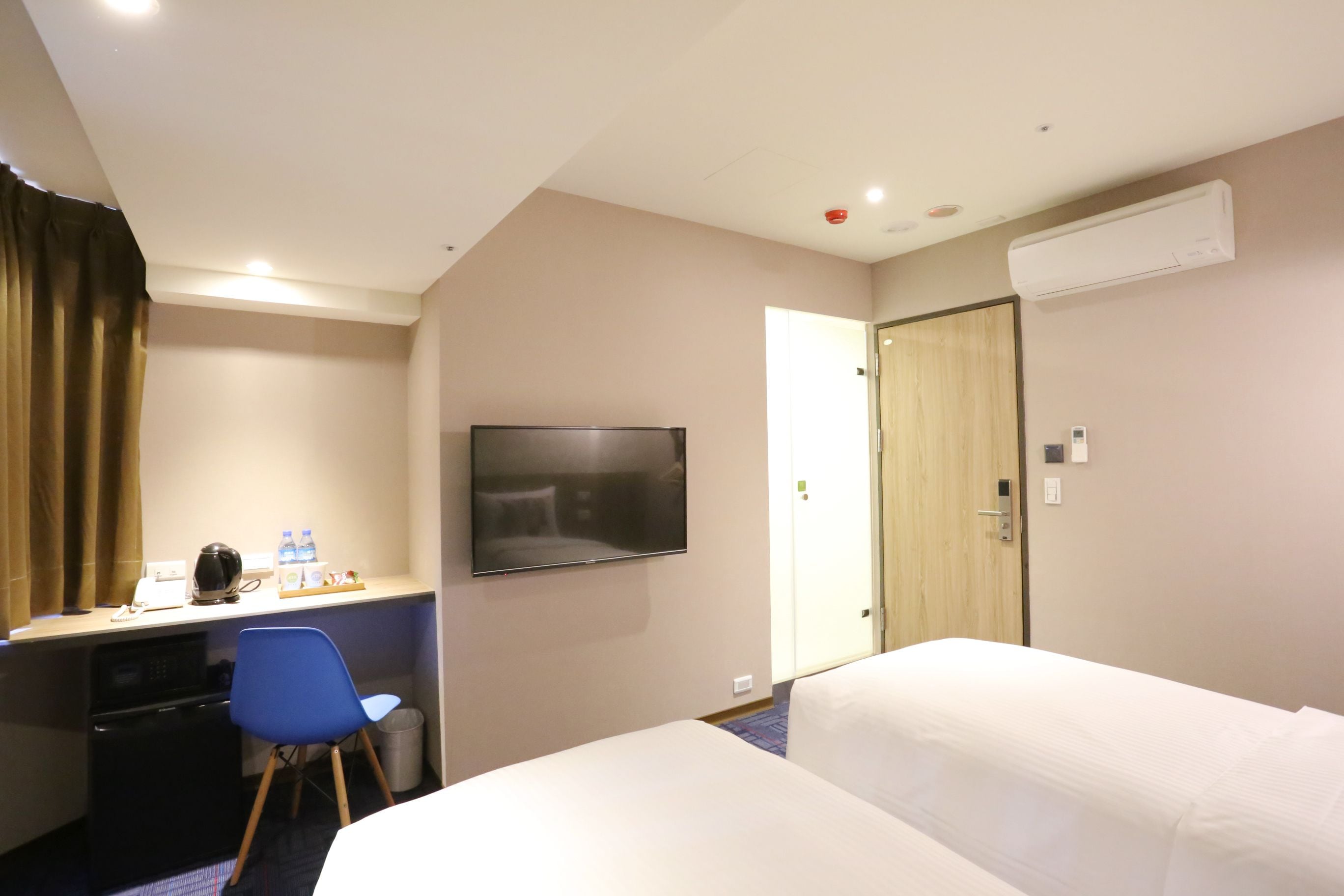 A hotel room with a bed, a desk with a chair, a television, and an air conditioning unit.