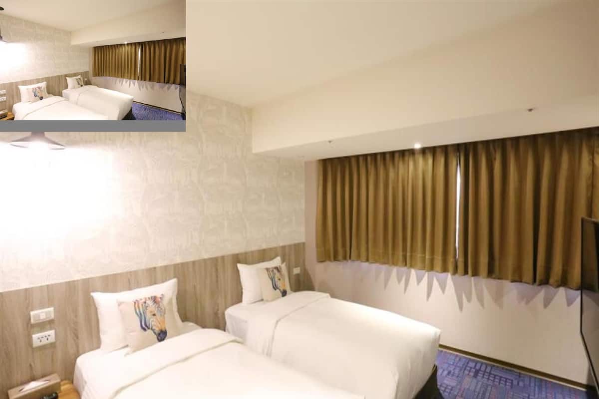A hotel room with two beds, a large window with curtains, a flat-screen TV, and a wall-mounted phone.
