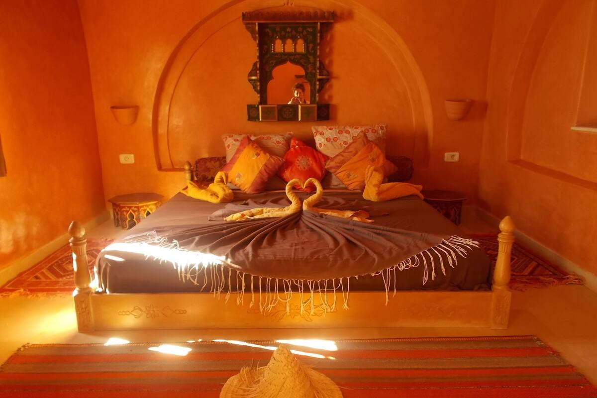 A bed with a decorative headboard, a woven basket, and a wall-mounted mirror.