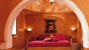 A cozy bedroom with a bed, pillows, a small table, and a hanging light fixture. - Maison Leila (Mezraia)