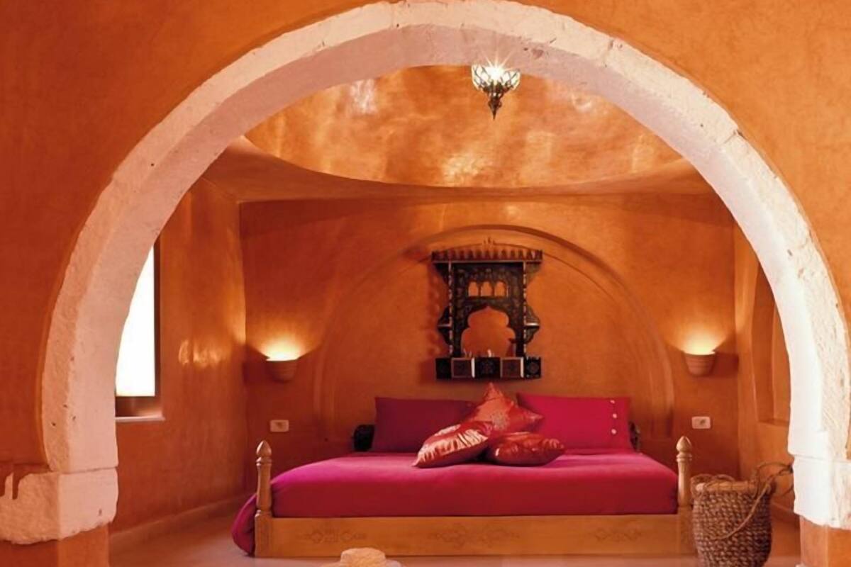 A cozy bedroom with a bed, pillows, a small table, and a hanging light fixture.