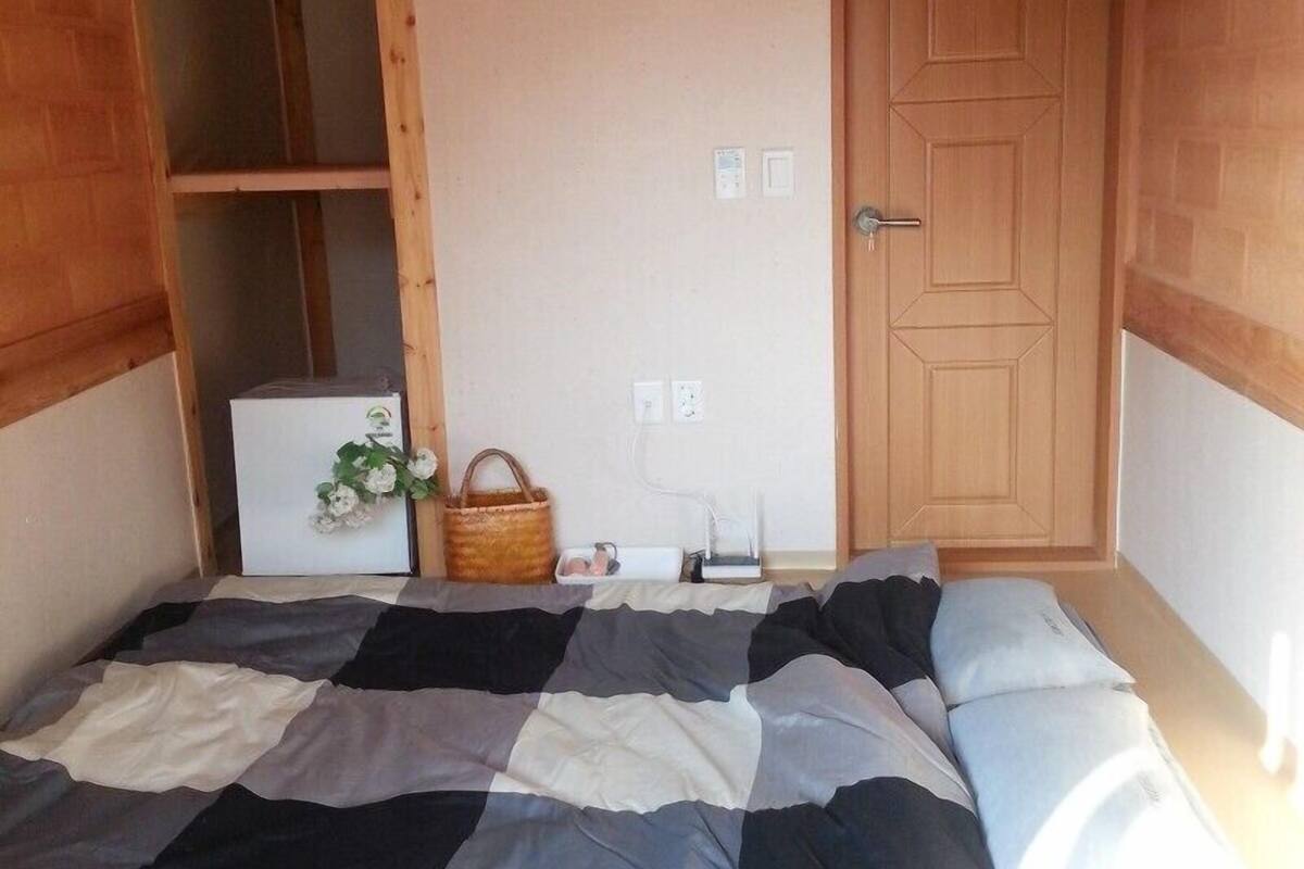 A bedroom with a bed, a wooden wardrobe, a door, and a wall socket.