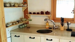 A kitchen with a sink, wooden shelves with dishes, and a window. - Happy Village Syeobul Guesthouse (Gyeongju)