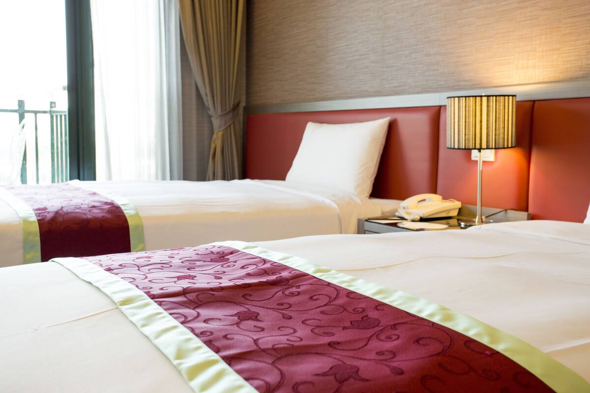 Habitació d'hotel amb dos llits, una taula de nit amb una làmpada i una finestra amb cortines.