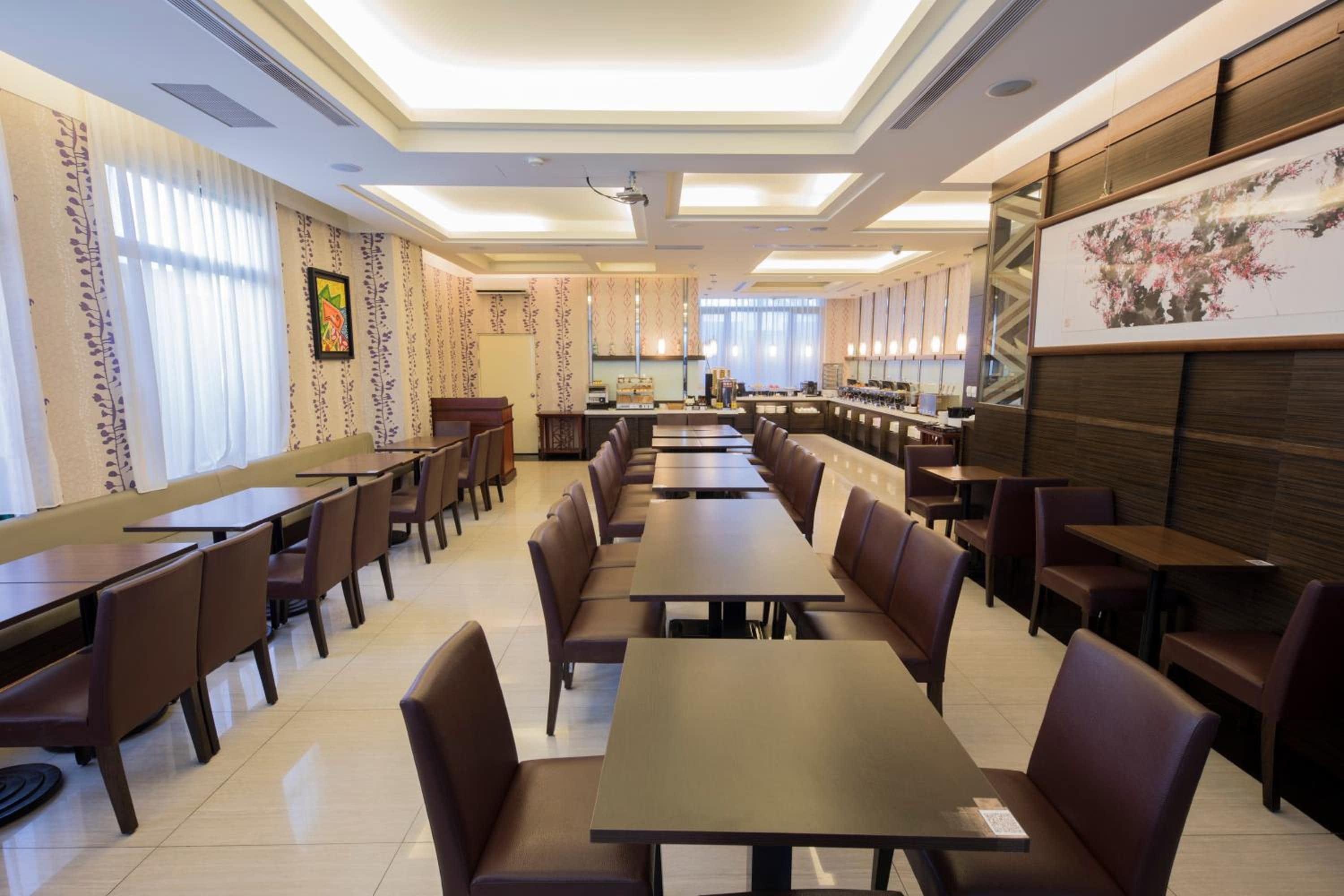 A restaurant with multiple dining tables and booths, a kitchen area, and a large painting on the wall.