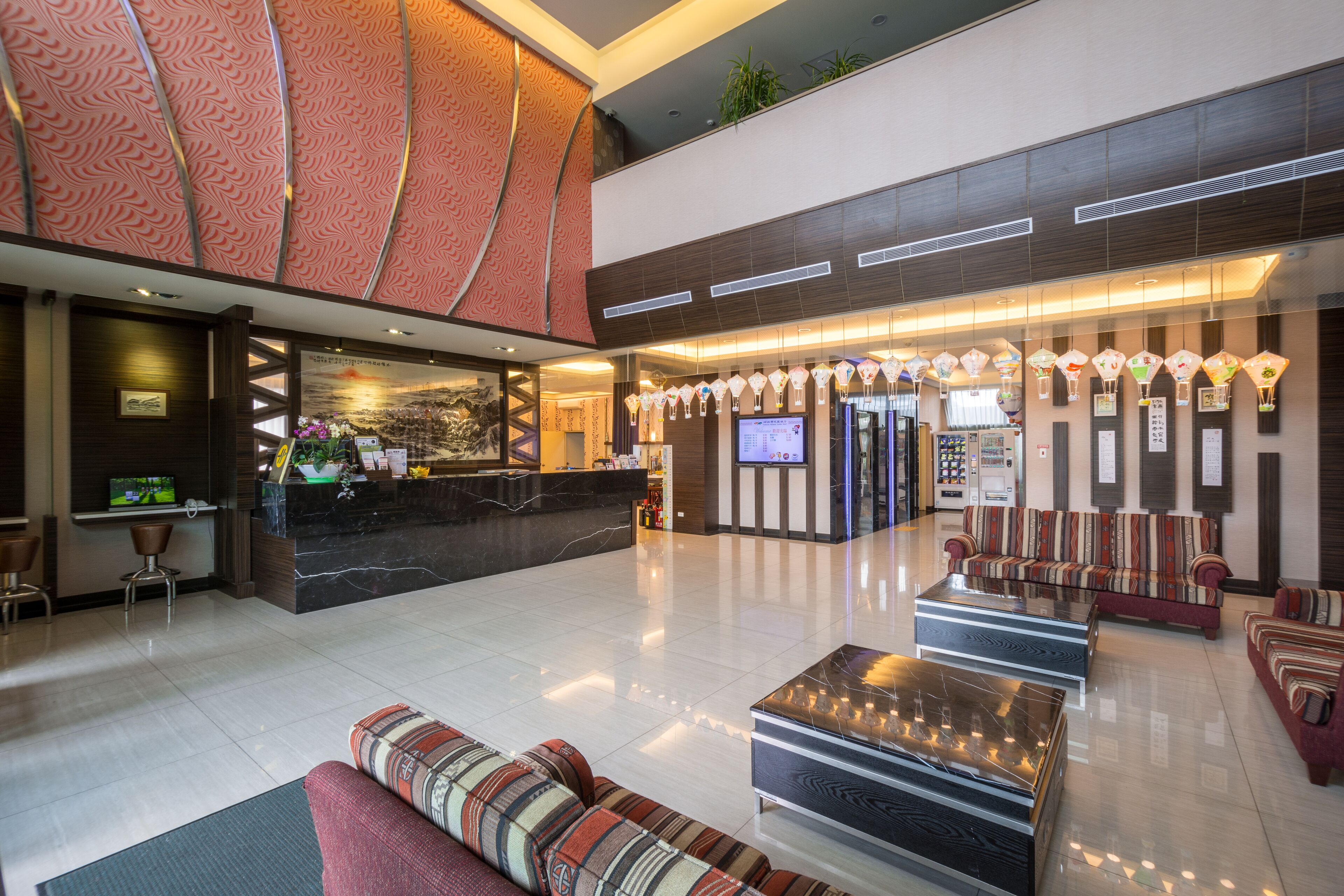 A hotel lobby with a reception desk, seating area, and a large screen.