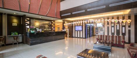 Um saguão de hotel com balcão de recepção, área de estar e uma tela grande.