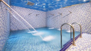 A swimming pool with a blue mosaic tile design and a ceiling that mimics a cloudy sky.