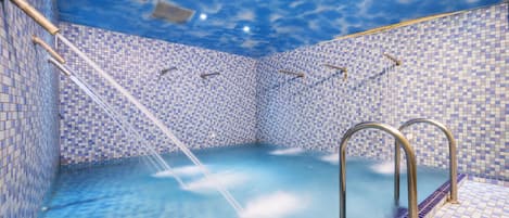 A swimming pool with a blue mosaic tile design and a ceiling that mimics a cloudy sky.