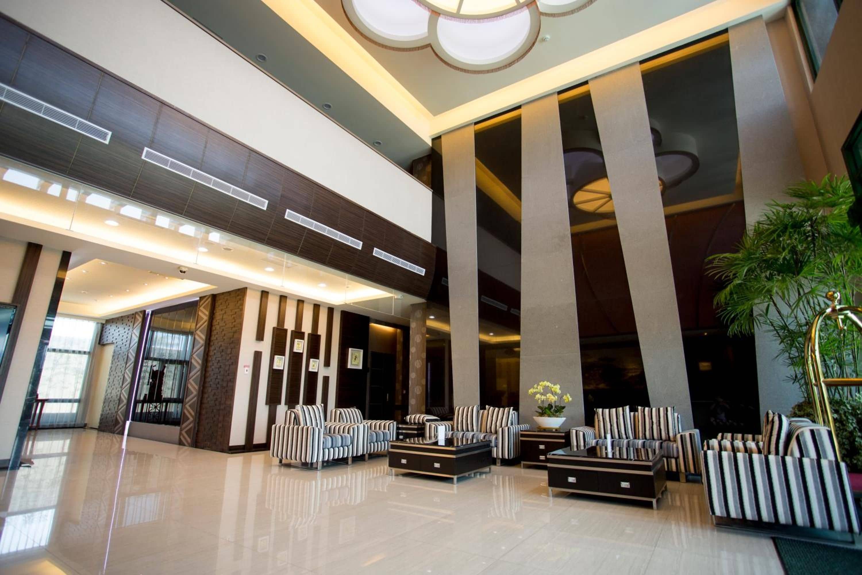 Un hall d’entrée moderne avec de hauts plafonds, de grandes fenêtres et un espace détente doté de canapés à rayures.