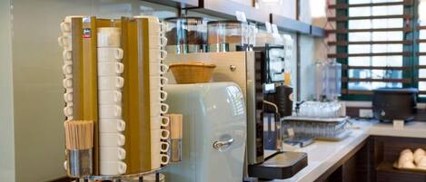 A coffee station with multiple coffee machines, a basket, and stacked plates.