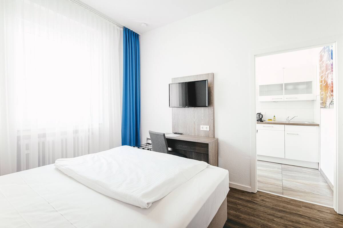 A hotel room with a bed, a desk, a TV, and a kitchenette.