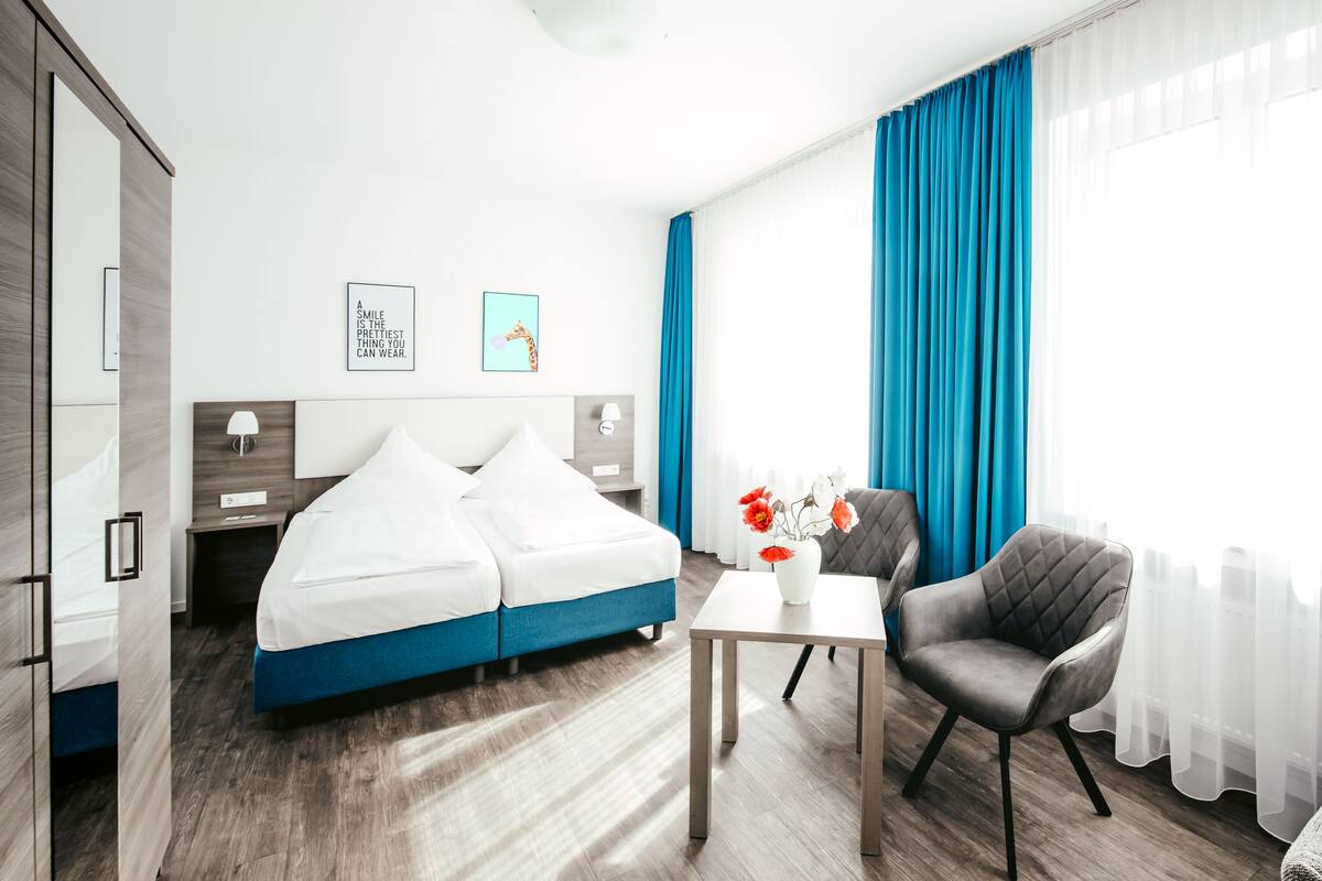 A modern hotel room with a double bed, a desk, a chair, and a vase with flowers.