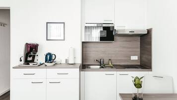 A modern kitchen with white cabinets, a built-in oven, and a sink. There is a coffee maker, a kettle, and a glass vase with a plant on the counter.