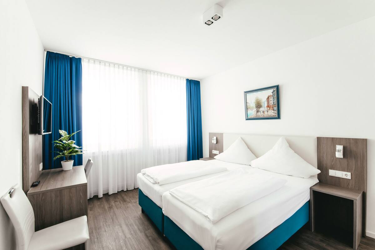 A hotel room with two beds, a desk, a chair, a TV, and a window with curtains.
